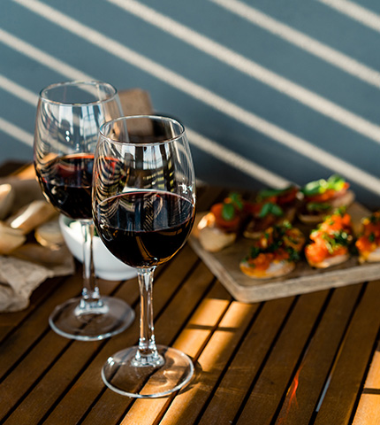 activite-2 Verres de vin rouge du Vignoble Montvinea servis sur une terrasse ensoleillée, accompagnés de bruschettas gourmandes pour un apéritif convivial.