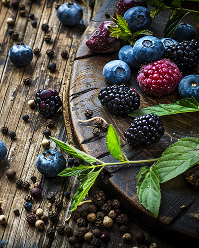 syrah Mûres, myrtilles et grains de poivre sur bois rustique illustrant la puissance aromatique du cépage Syrah.